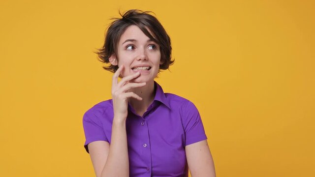Pensive thoughtful confused shy shamed short hairdo young woman 20s years old in pink violet shirt looking camera spreading hands say oops oh ouch i am so sorry isolated on yellow background studio