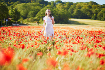 Beautiful young woman in white dress walking in poppy field on a summer day