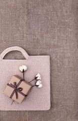 Beige knitted handmade bag, eco gift box and cotton flowers with brown burlap background. Eco-friendly shopping. Zero waste lifestyle. Top view, copy space