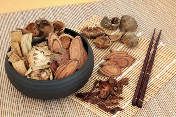 Traditional dried chnese herbs used in herbal medicine in a bowl, loose & with chopsticks on bamboo. Alternative healthcare concept.