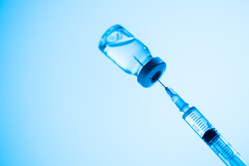 Vial and syringe of coronavirus vaccine, medicine in blue studio light, copy space. Vaccination...