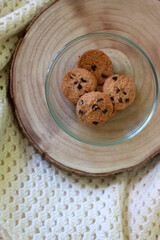 Bowl of chocolate chip cookies, wooden tray and knitted blanket. Flat lay.