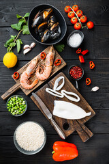 Spanish seafood paella ingredients, rice,prawns, mussels, peas on  black wooden background, flat lay