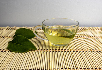 Bilberry tea, Peumus boldus, in a clear glass cup on a bamboo mat on a light background and leaves on the side. Used for medicinal purposes and for digestive support.