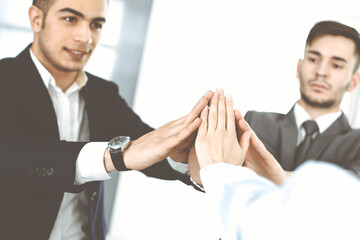 Business people group showing teamwork, joining hands and giving five to each other in modern office. Success concept