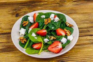 Fresh healthy salad with strawberry, spinach, walnuts and feta cheese on wooden table
