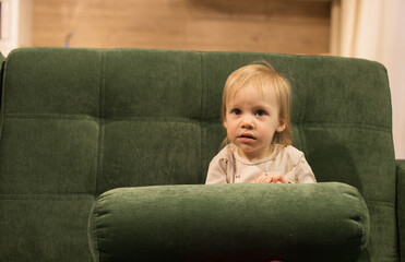 portrait of a blonde girl with big blue eyes in close-up, who sits on the sofa and looks with interest