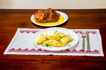 Ukrainian food vareniki, pierogi on wooden table over typical Ukrainian towel with roasted meat