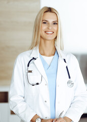 Woman-doctor at work in clinic happy of her profession. Blond female physician controls medication history record and medical exam results. Medicine concept