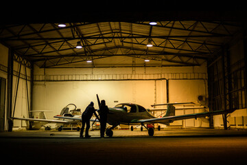 two men parking small jet in a hangar at night