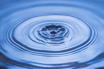 View of drops making circles on blue water surface isolated on background.