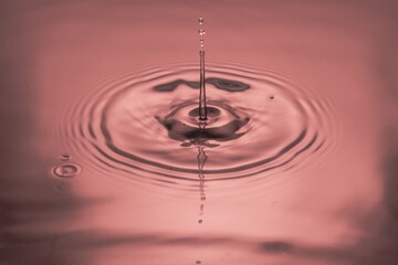 Close up view of Drops making circles on blue water surface isolated on red background.