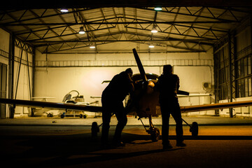 two men parking small jet in a hangar at night