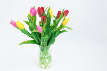 A bouquet of flowers on a white background. Multicolored tulips stand in a transparent jug. Festive mood. There is room for text