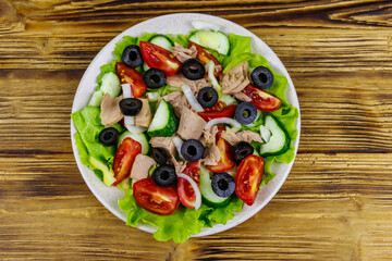 Tasty tuna salad with lettuce, black olives and fresh vegetables on wooden table. Top view