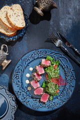 Slices of tuna in sesame seeds on blue ceramic plate. Vertical photo. Top view. Dark blue textured background. Dietary nutrition.
