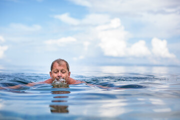 Fototapeta na wymiar Senior man swimming in the Sea/Ocean - enjoying active retirement, having fun, taking care of himself, staying fit
