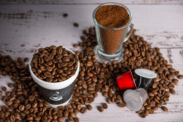 Distintos tipos de cafe, crudo, tostado, molido y en capsulas en varios recipientes.