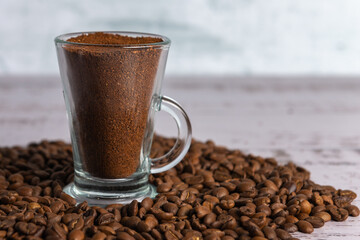 Vaso de vidrio transparente con café molido en su interior sobre granos de café 