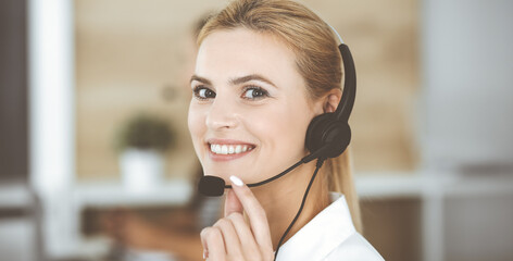 Blonde business woman using headset for communication and consulting people at customer service office. Call center. Group of operators at work