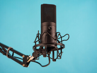 Studio condenser microphone close-up. It is mounted on a black stand. Concept - equipment for radio broadcasting. Microphone radio presenter on a blue background. Broadcast studio microphone.