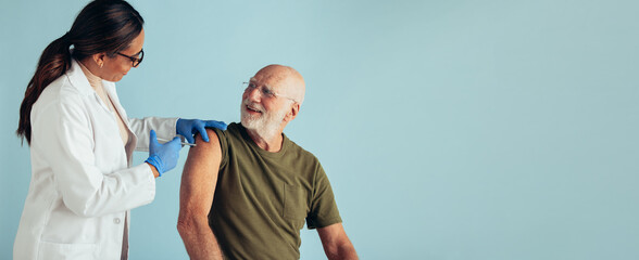 Senior man getting vaccinated on blue background - obrazy, fototapety, plakaty