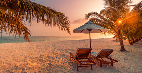 Beautiful tropical sunset scenery, two sun beds, loungers, umbrella under palm tree. White sand, sea view with horizon, colorful twilight sky, calmness and relaxation. Inspirational beach resort hotel