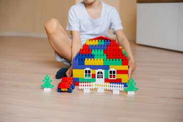 A little boy plays with a construction kit and builds a big house for the whole family. Construction of a family home.