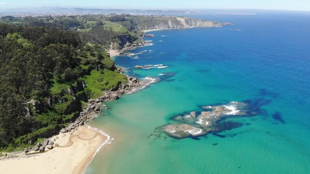 turquoise blue sea and stone cliff with lush green vegetation, La &Ntilde;ora beach, Villaviciosa, Gij&oacute;n, Asturias, Spain.
