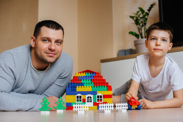 Fototapeta premium A little boy together with his father is played by a constructor and builds a house. Construction of a family home.