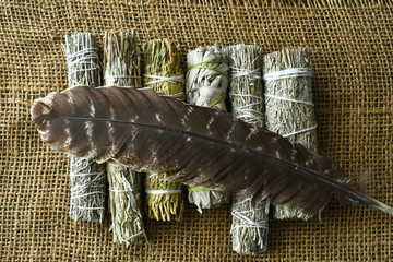 A top view image of a variety of healing smudge bundles with sacred feather on burlap. 