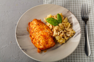Baked chicken breast on a gray plate with pineapple salad on a table on a napkin on a concrete background near a fork.