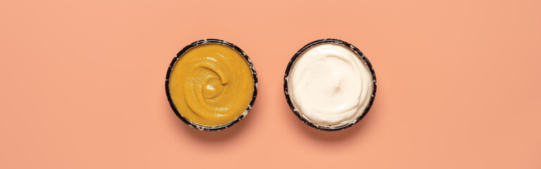 Mustard and mayonnaise in a bowl on a pink pastel background, banner. Top view.