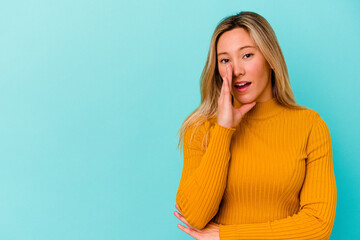 Young mixed race woman isolated on blue background is saying a secret hot braking news and looking aside