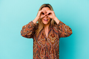 Young mixed race woman isolated on blue background showing okay sign over eyes