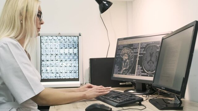 Professional female doctor radiologist examines brain CT or MRI scan results, working on a computer screen at her personal desk at hospital