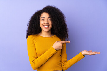Young african american woman isolated on purple background holding copyspace imaginary on the palm...