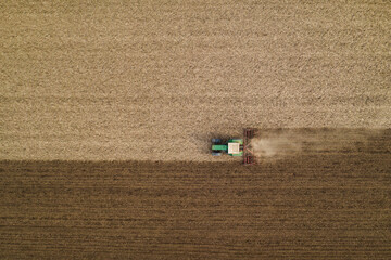 Aerial view of agricultural tractor tilling and harrowing ploughed field, directly above drone pov