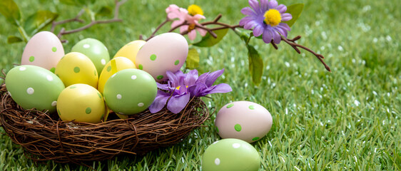 Fototapeta na wymiar Happy Easter. Pastel colored eggs in a nest on green grass, close up view