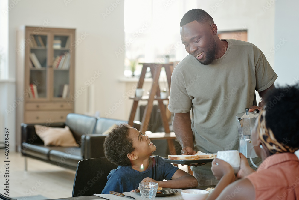 Canvas Prints Happy young father and cute little son looking at one another during breakfast by kitchen table