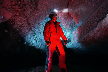 Fototapeta na wymiar A guy in an ice cave with a lantern light. The caver descended into the ice cave. Snow stalactites and ice walls. In some places there are stones. Colored lantern beams. Bogdanovich Glacier, Almaty