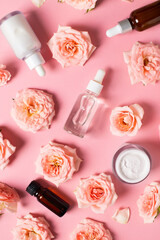 Bottles of serum and cream tube with rose flowers flat lay on pink background