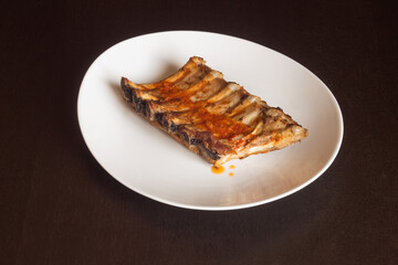 Presentation of plating food of baked pork ribs bathed in a sauce of garlic, oil, vinegar, and oregano on a white dish. Cooked recipes with meat.