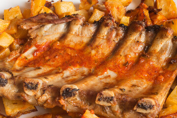 Obraz na płótnie Canvas Detail of baked pork ribs with garlic sauce, oil, vinegar, and spicy spices surrounded by potatoes. Fresh food and barbecue meats.