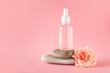 Bottle of facial serum on stone with rose flower on pink background