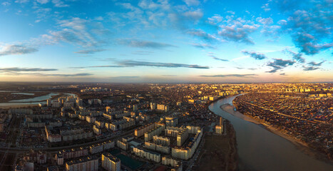 Obraz premium evening panoramic landscape of one- and multi-storey buildings and streets of the city of Krasnodar in the rays of the setting sun with blue sky and beautiful clouds
