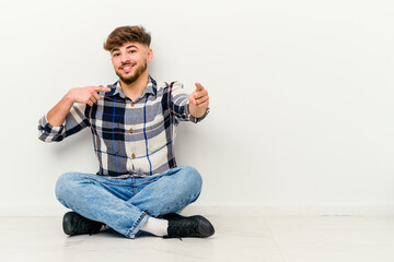 Young Moroccan man sitting on the floor isolated on white background pointing to front with fingers.
