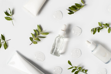 Bottles of serum with green leaves flat lay on white background