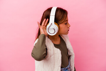 Fototapeta premium Little caucasian girl listening music isolated on pink background trying to listening a gossip.