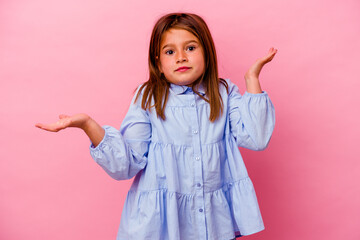 Little caucasian girl isolated on pink background  doubting and shrugging shoulders in questioning...